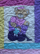 Quilt with teddy bear design in purple, blue, and pink on a white background